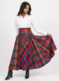 A woman modeling a high-waisted, full-length flared skirt in a vibrant multicolor tartan plaid pattern. The skirt features a lace-up corset waistband.