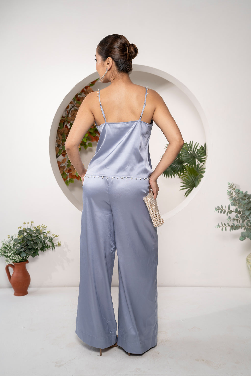 Woman wearing a light blue Azure Whisper Satin Co-ord Set – Pearl Strap Camisole & Wide-Leg Pants with a white background and decorative elements.