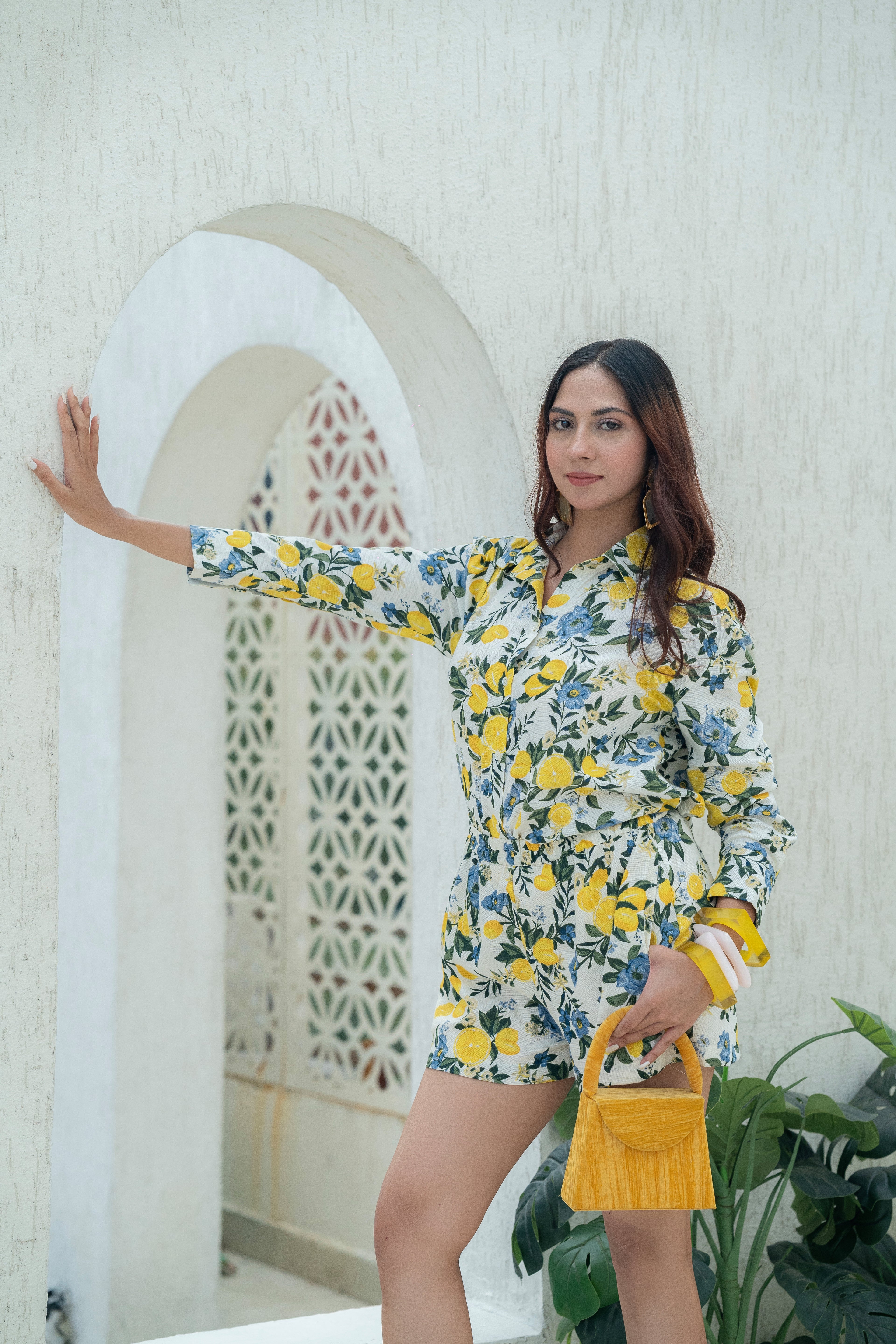 Woman in a Citrus Bloom Oversized Shirt & Shorts Co-ord Set – Printed Cotton Flax Resort Wear with a yellow handbag standing in front of a decorative archway.
