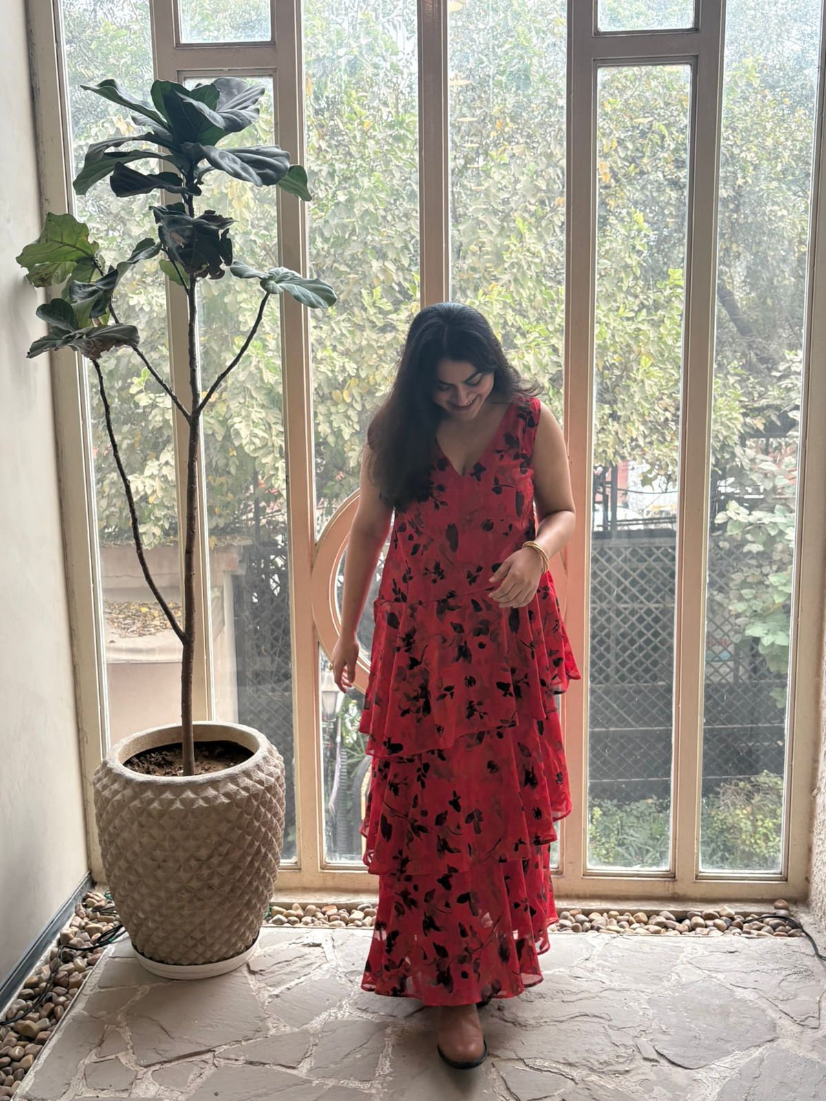Woman in a red dress standing in front of a large window with a plant to her left.