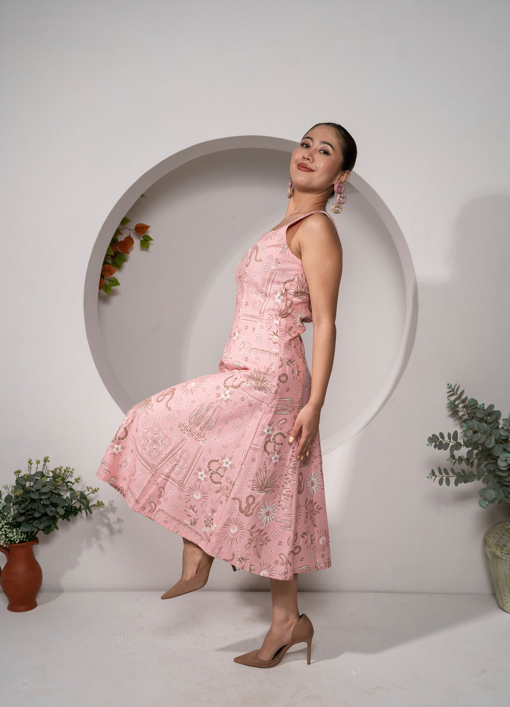 Woman in a Desert Rose – Western Pink Panelled Midi Dress standing in front of a white wall with decorative plants.
