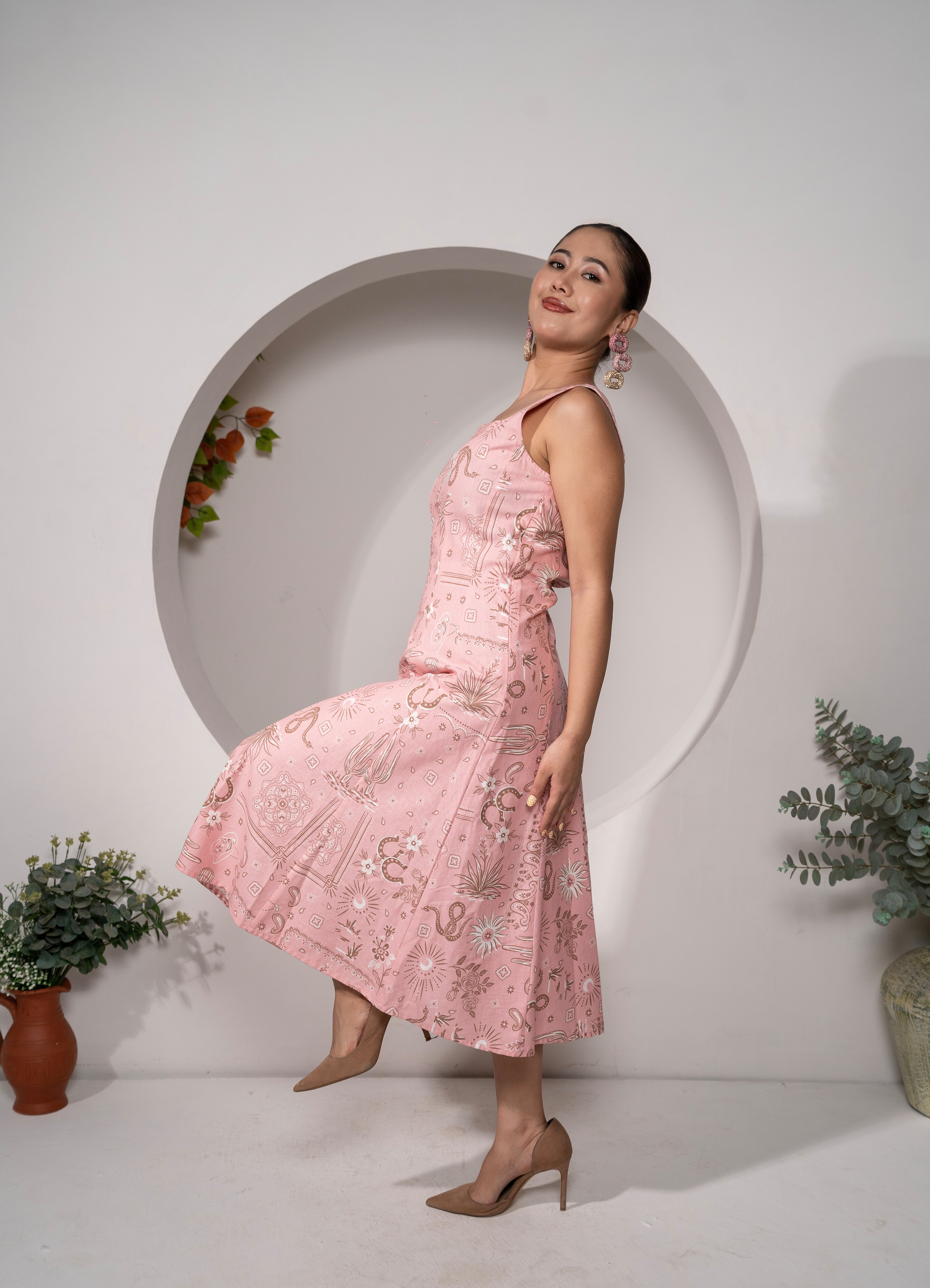 Woman in a Desert Rose – Western Pink Panelled Midi Dress standing in front of a white wall with decorative plants.