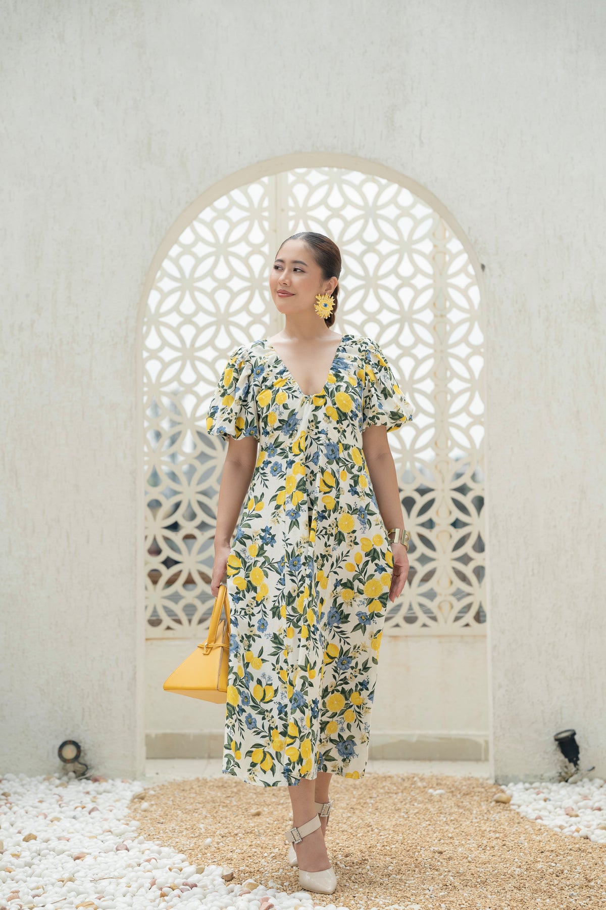 Khamna Citrus Bloom Puff Sleeve Dress in Cotton Flax Fabric in Lemon and blue floral Print standing in front of a decorative archway during Vacation. Resort wear Dress