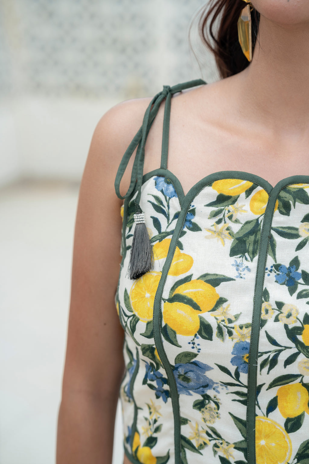 Close-up of a blue floral Khamna Amalfi Bloom Top – Scallop Detail Tassel Strap Crop with yellow lemons and green leaves on a blurred background