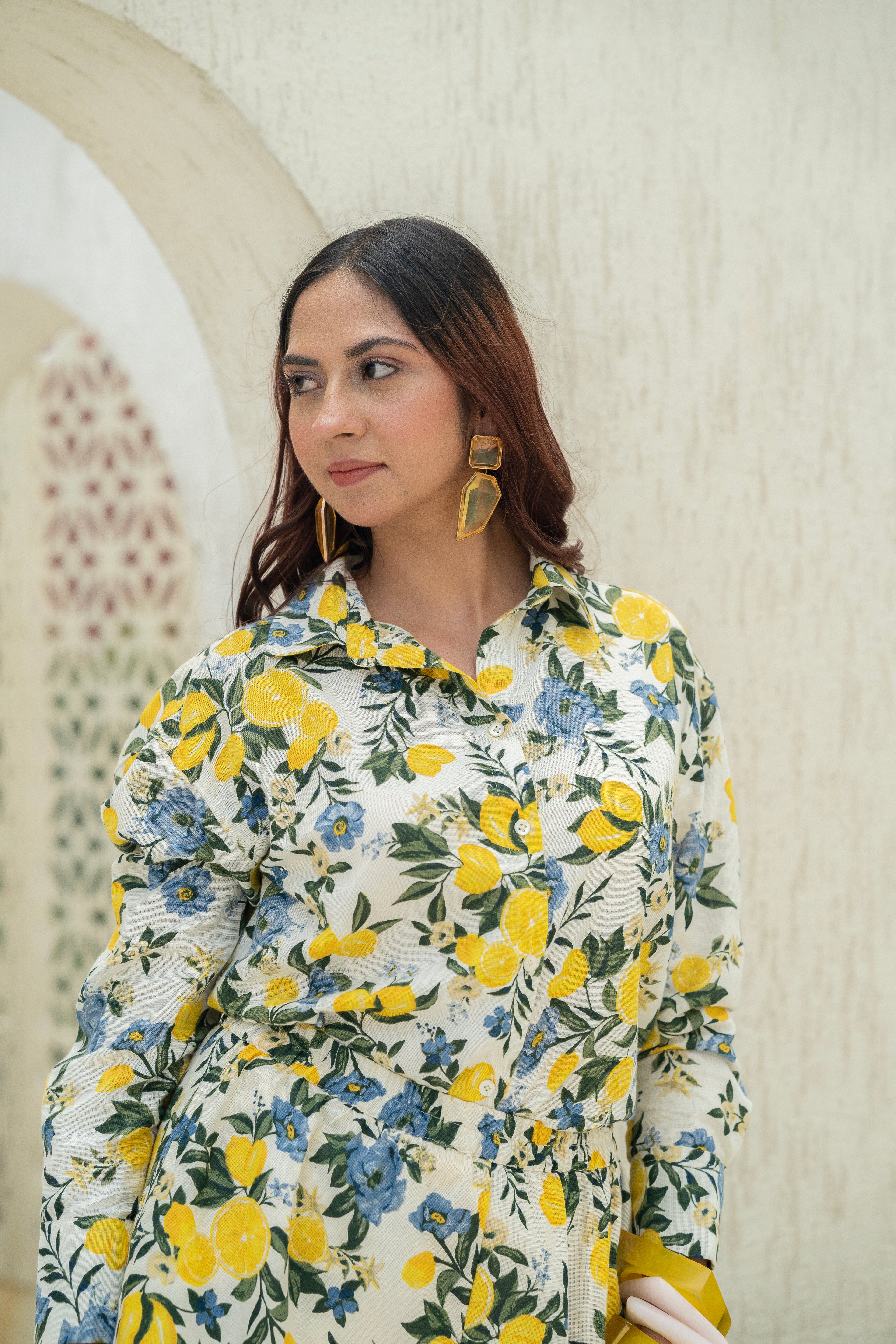 Woman wearing Khamna's Citrus Bloom Oversized Shirt – Printed Cotton Flax with yellow lemon and blue flowers against a neutral background