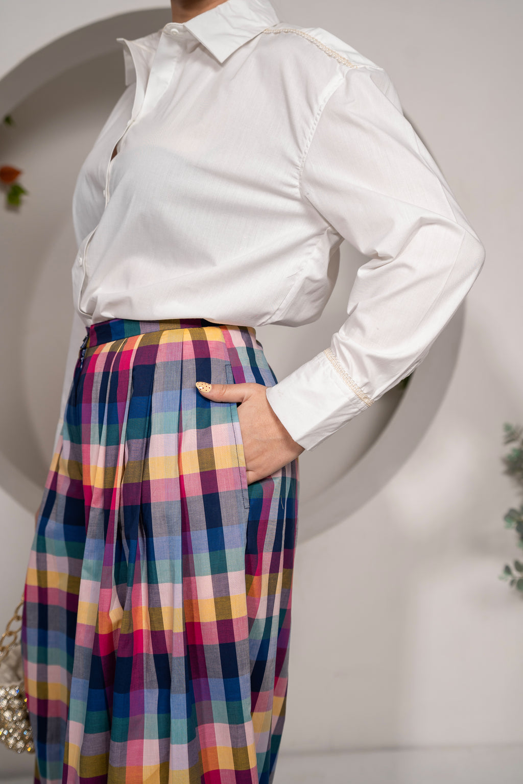 Person wearing a Khamna Cloudlight Oversized Shirt – White Cotton Poplin with Sparkle Lace and colorful plaid skirt against a neutral background