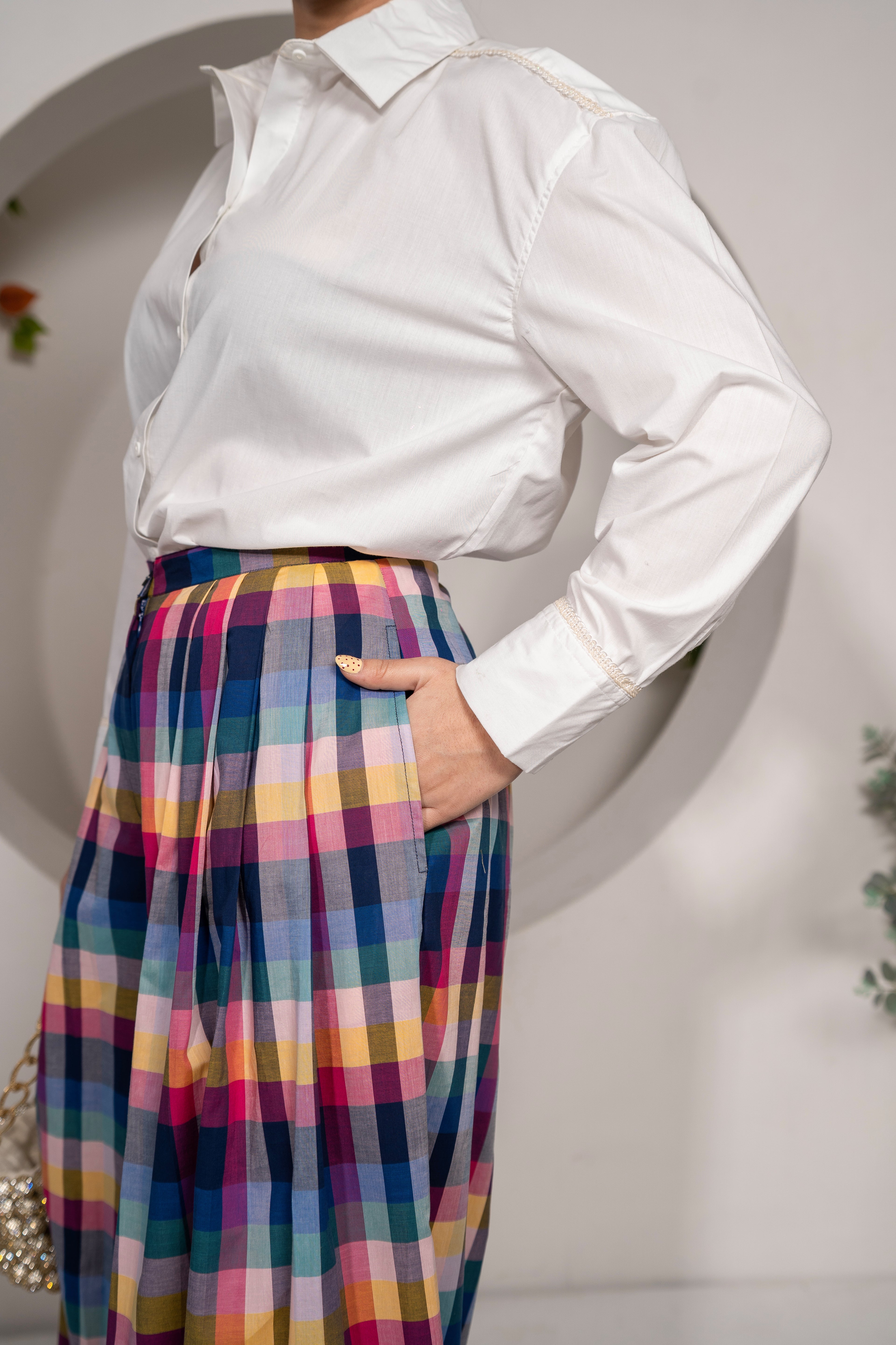 Person wearing a Khamna Cloudlight Oversized Shirt – White Cotton Poplin with Sparkle Lace and colorful plaid skirt against a neutral background