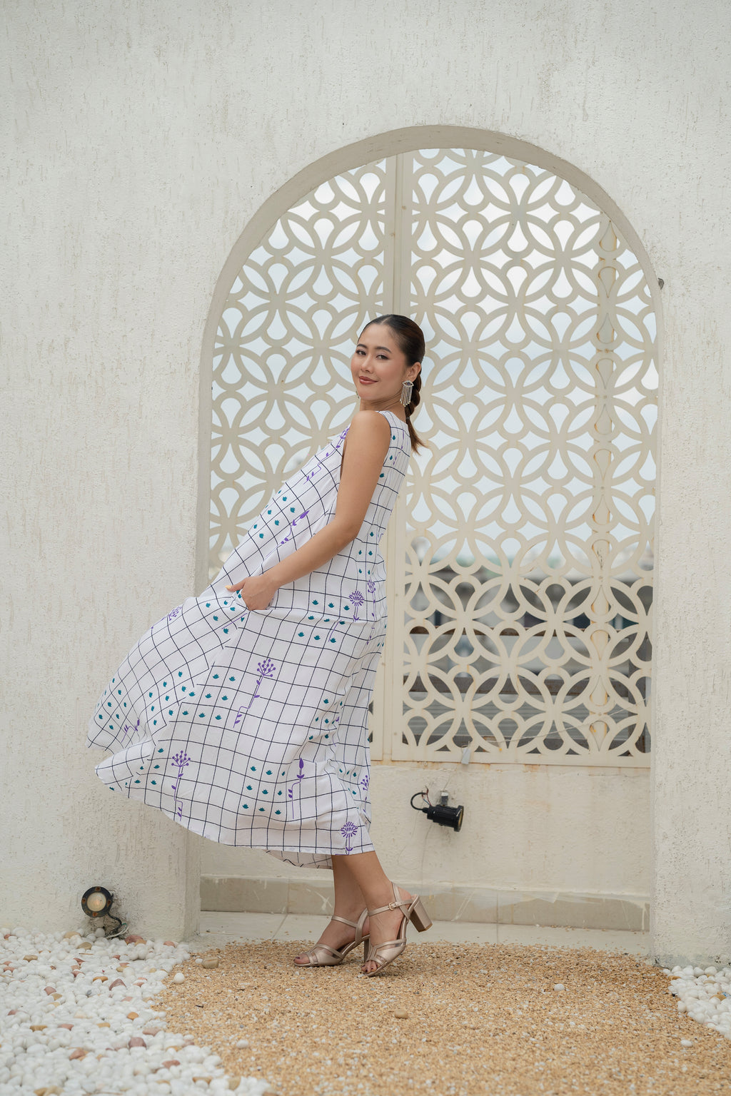 Woman in a checkered dress standing in front of a decorative stone wall.