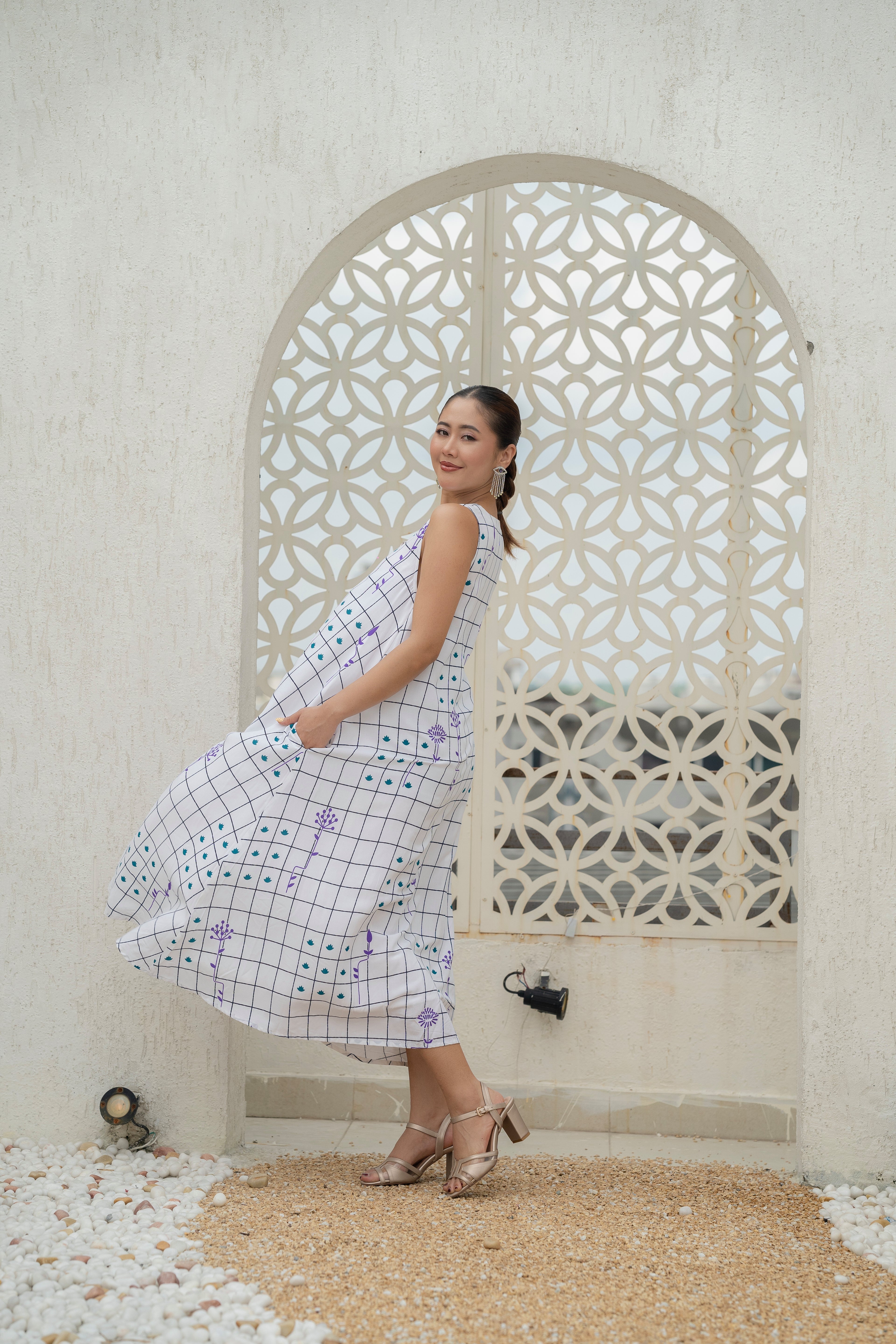 Woman in a checkered dress standing in front of a decorative stone wall.