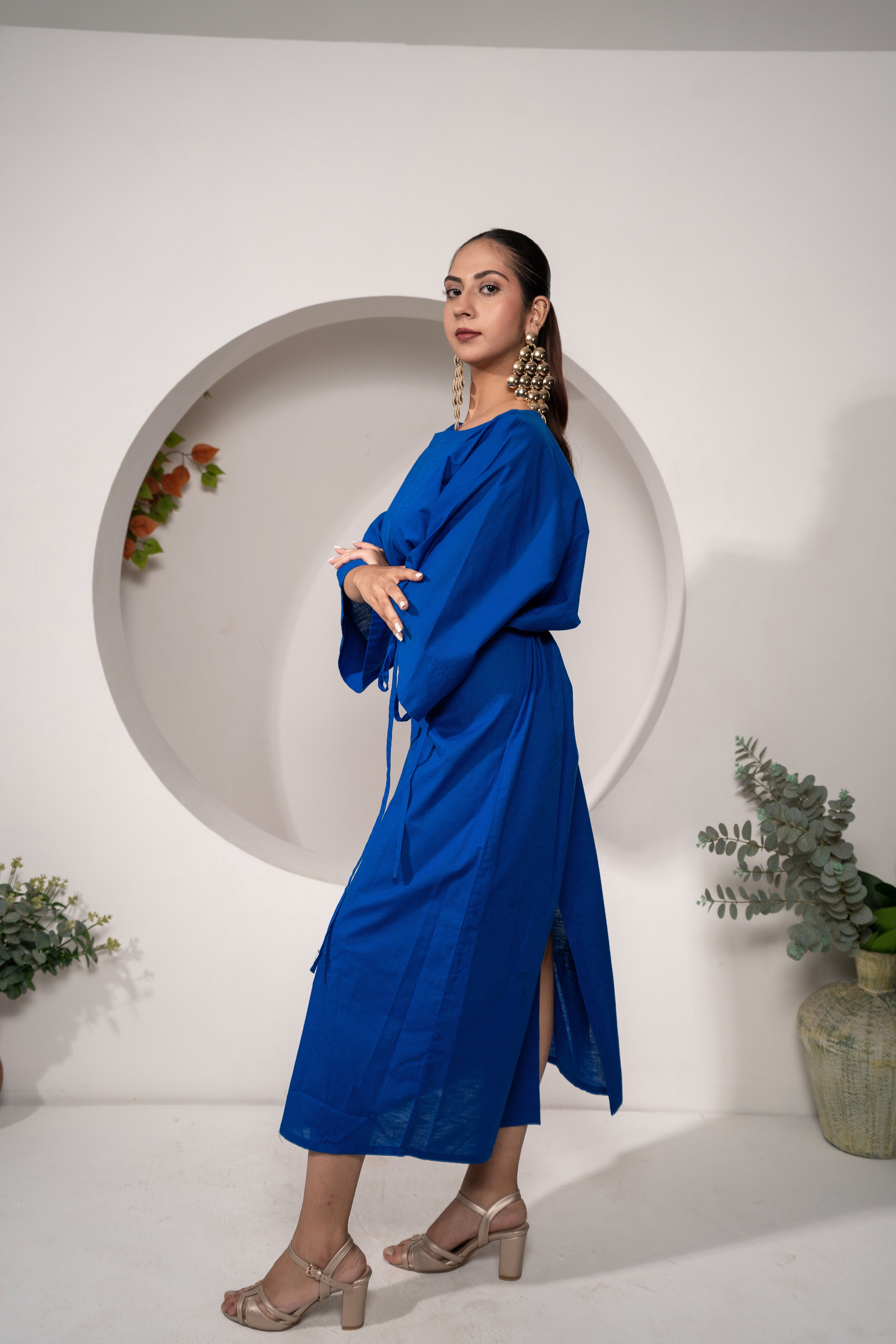 Woman in a Khamna's Ocean Mirage Kaftan Dress – Cotton Linen Tieable Drape posing in a minimalistic setting with plants.