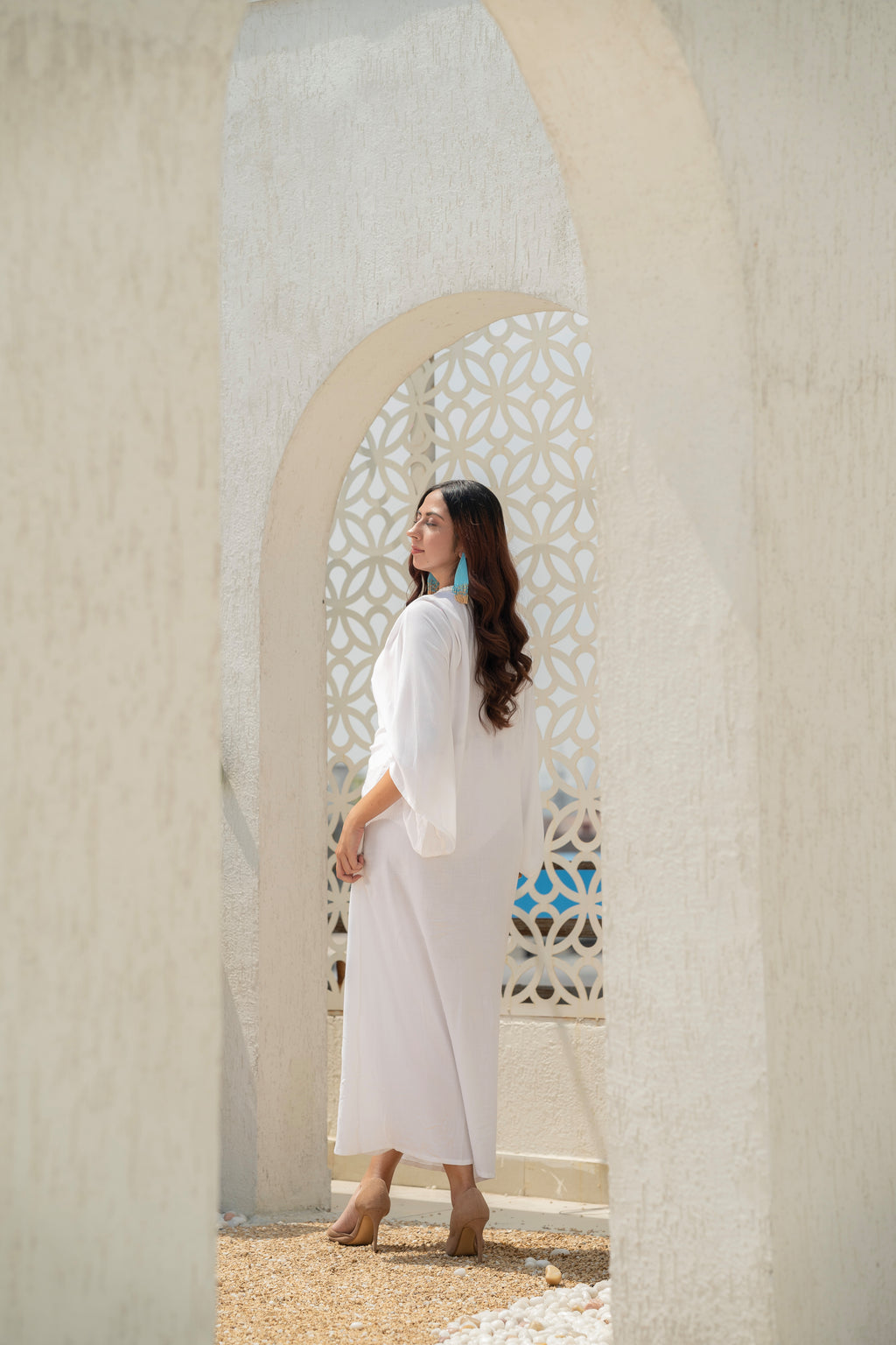 Woman in aKhamna Serenity Kaftan – White Vacation Cover-Up standing in front of a decorative archway.