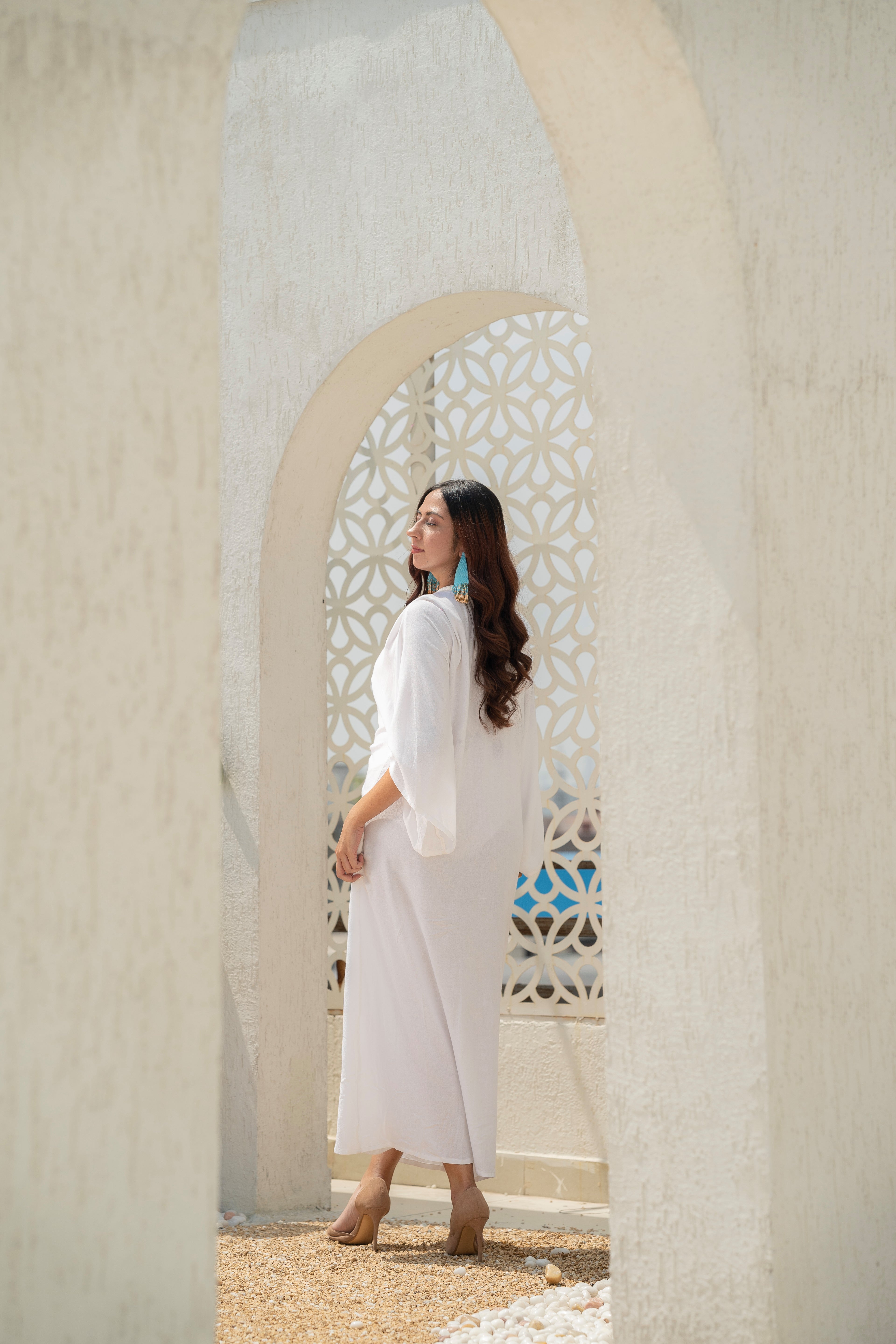 Woman in aKhamna Serenity Kaftan – White Vacation Cover-Up standing in front of a decorative archway.