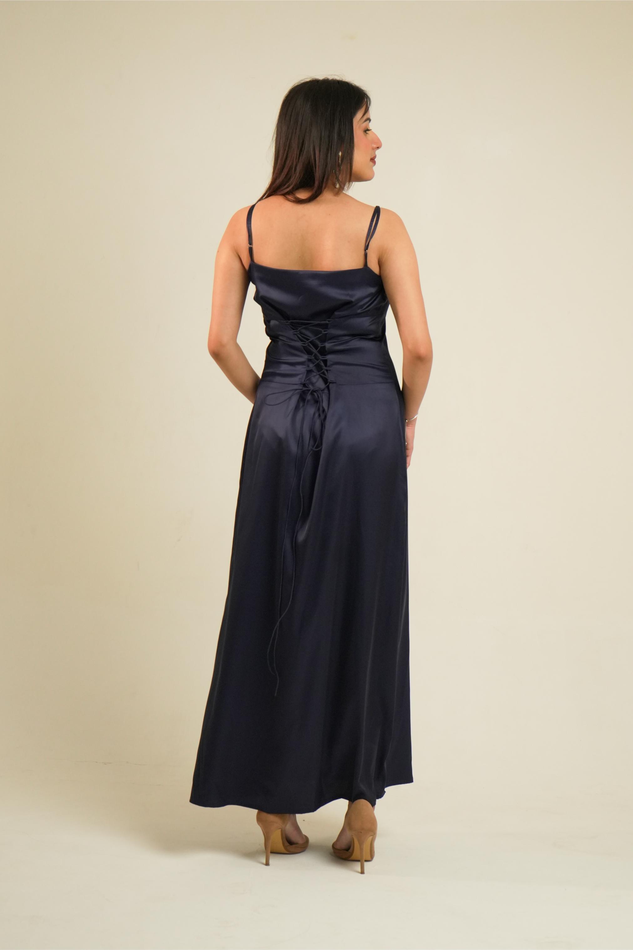A woman wearing a navy blue satin maxi dress, shown from the back against a plain beige studio background.