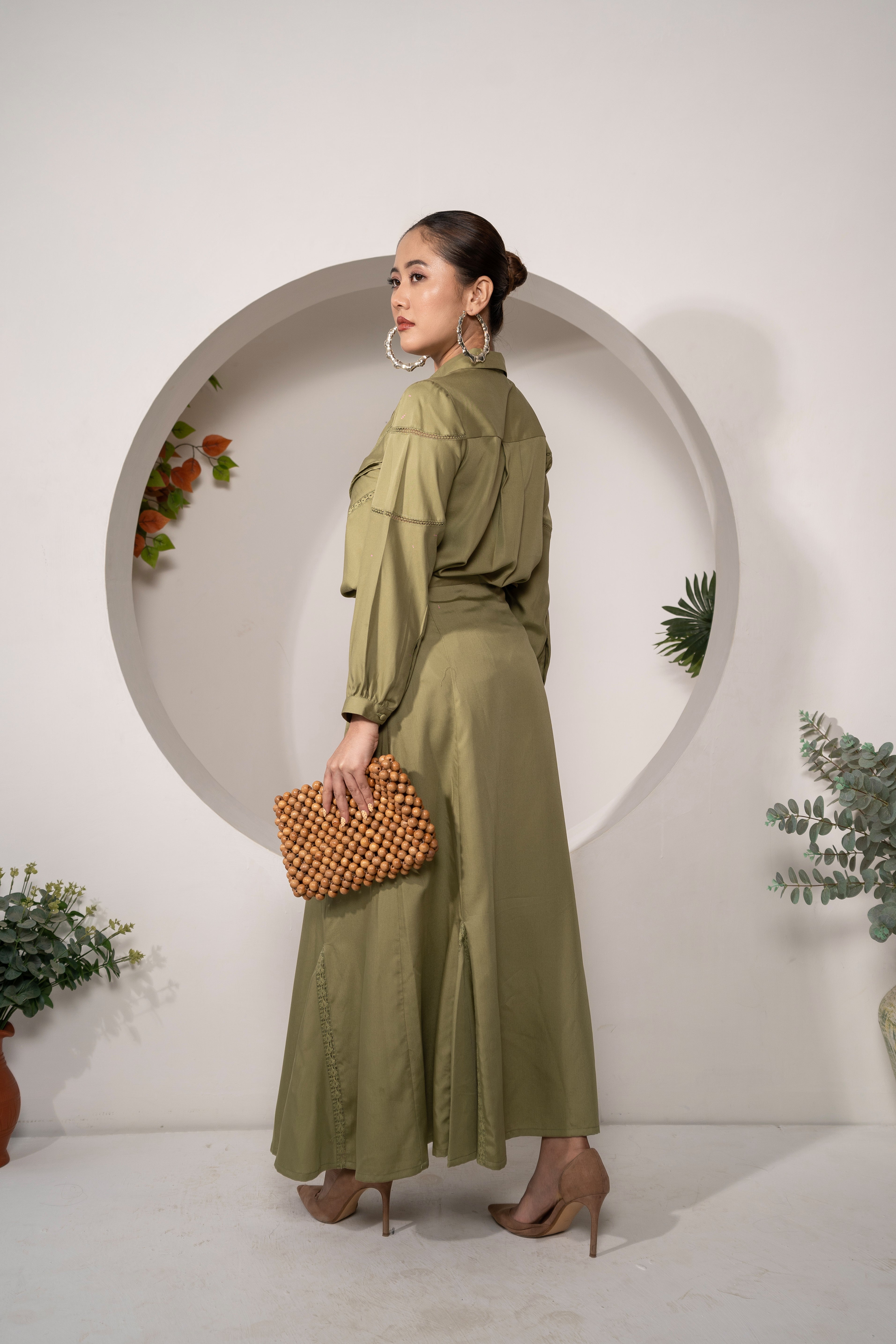Woman in a Olive Reverie – Lace Detail Modal Shirt with matching holding a clutch against a white wall with decorative elements.