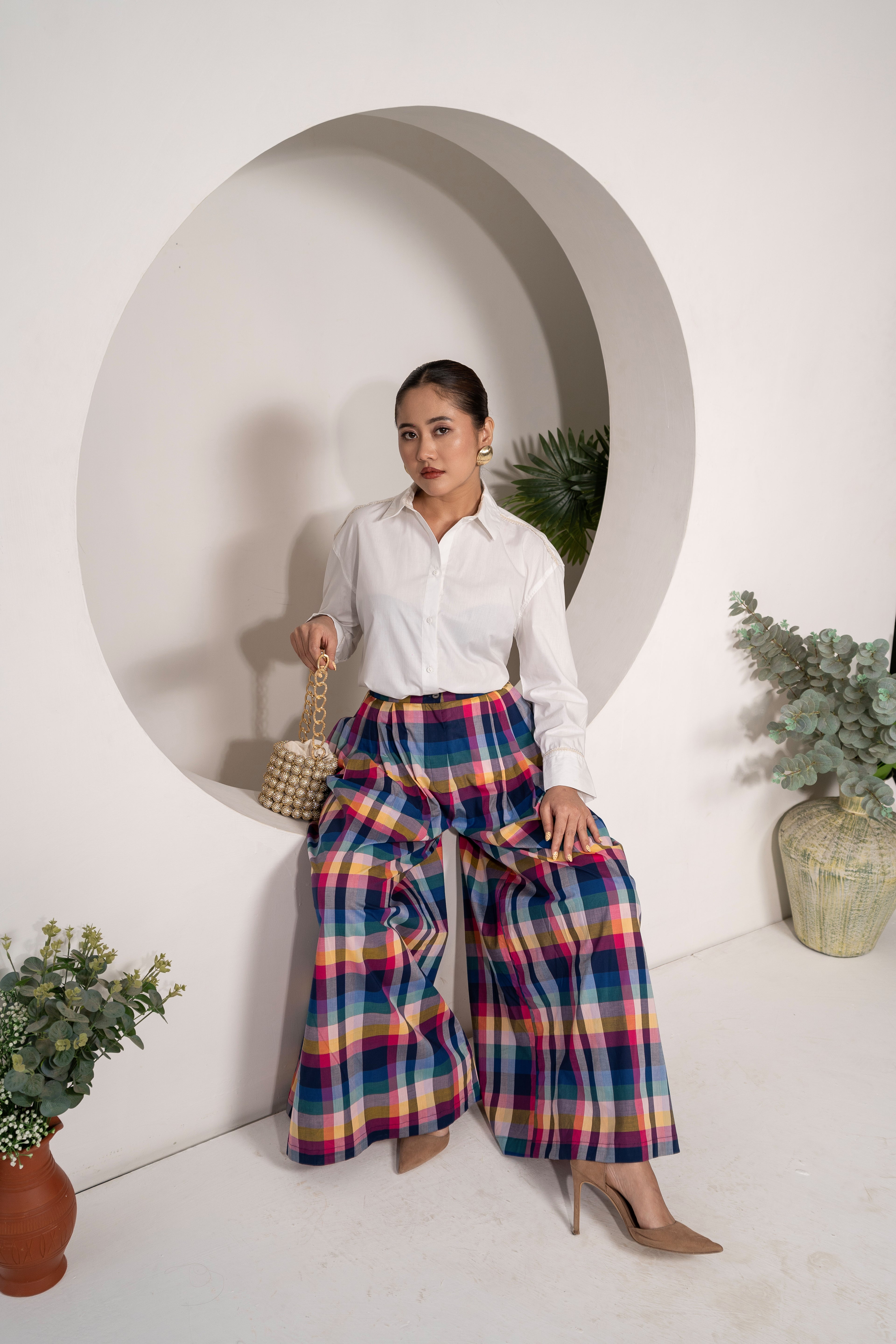 Woman wearing a white shirt and colorful plaid pants standing in a modern interior setting.