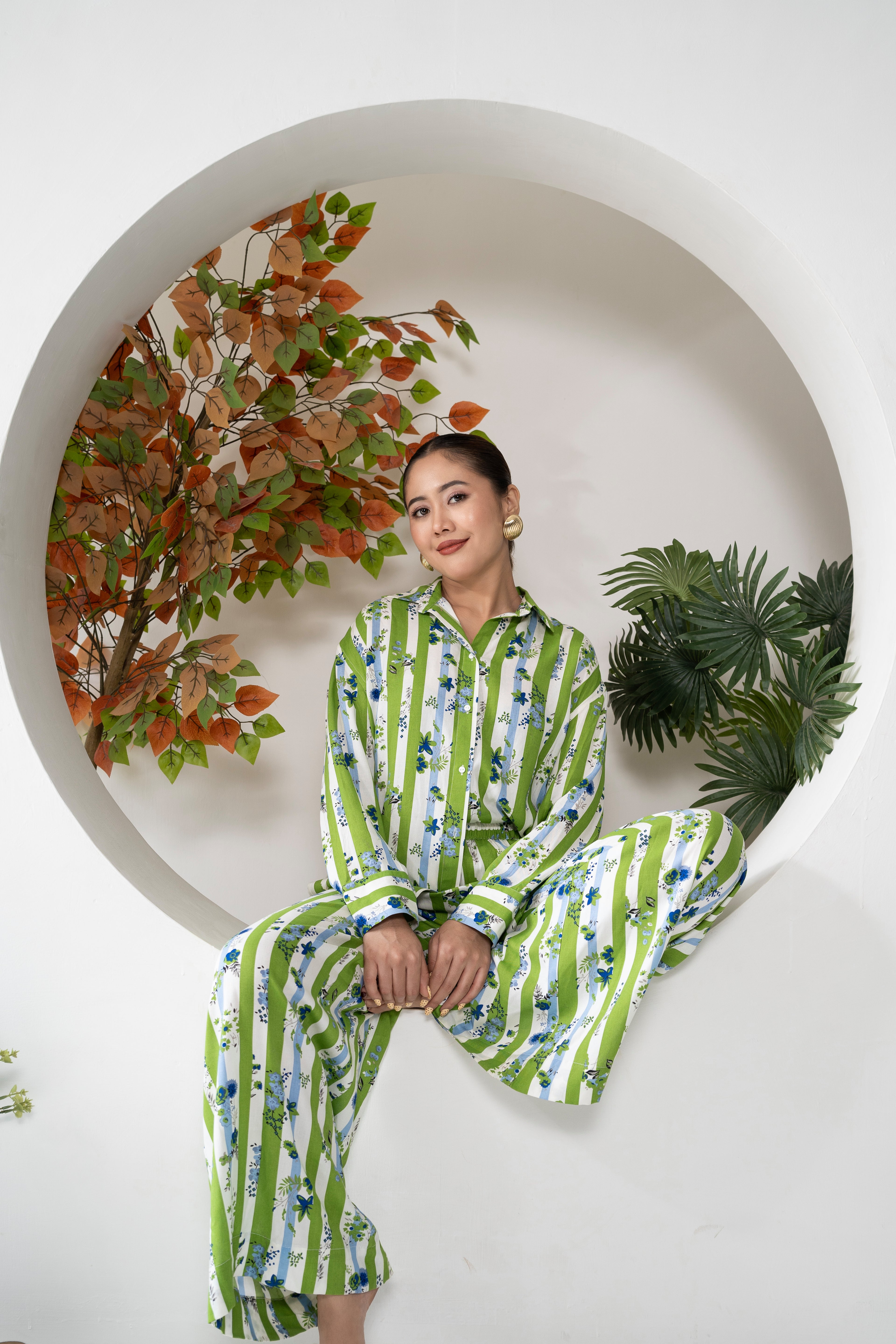 Woman in a green and white striped outfit sitting in a circular alcove with decorative plants.