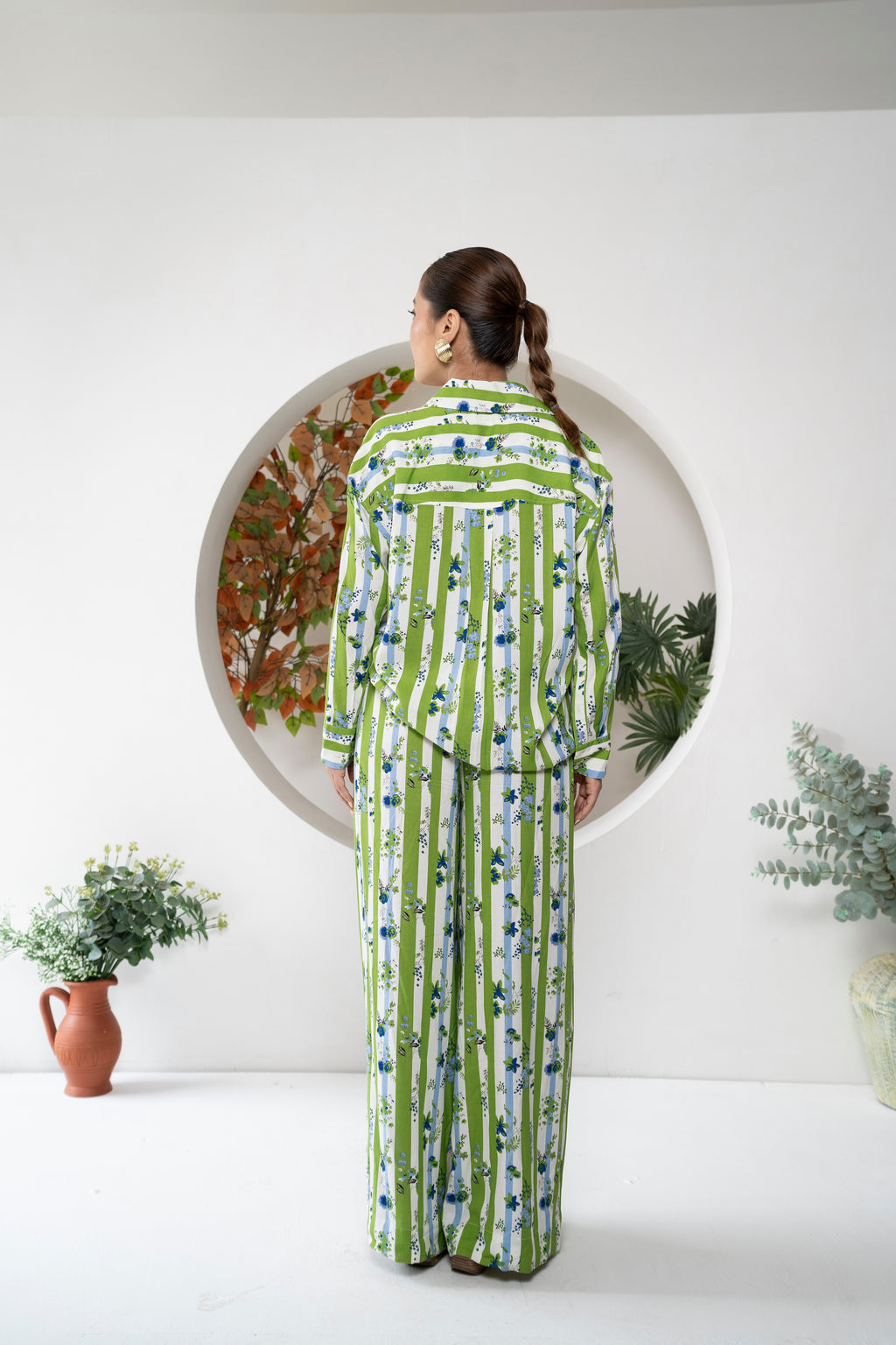 Woman wearing a green and blue patterned outfit standing in front of a decorative mirror.