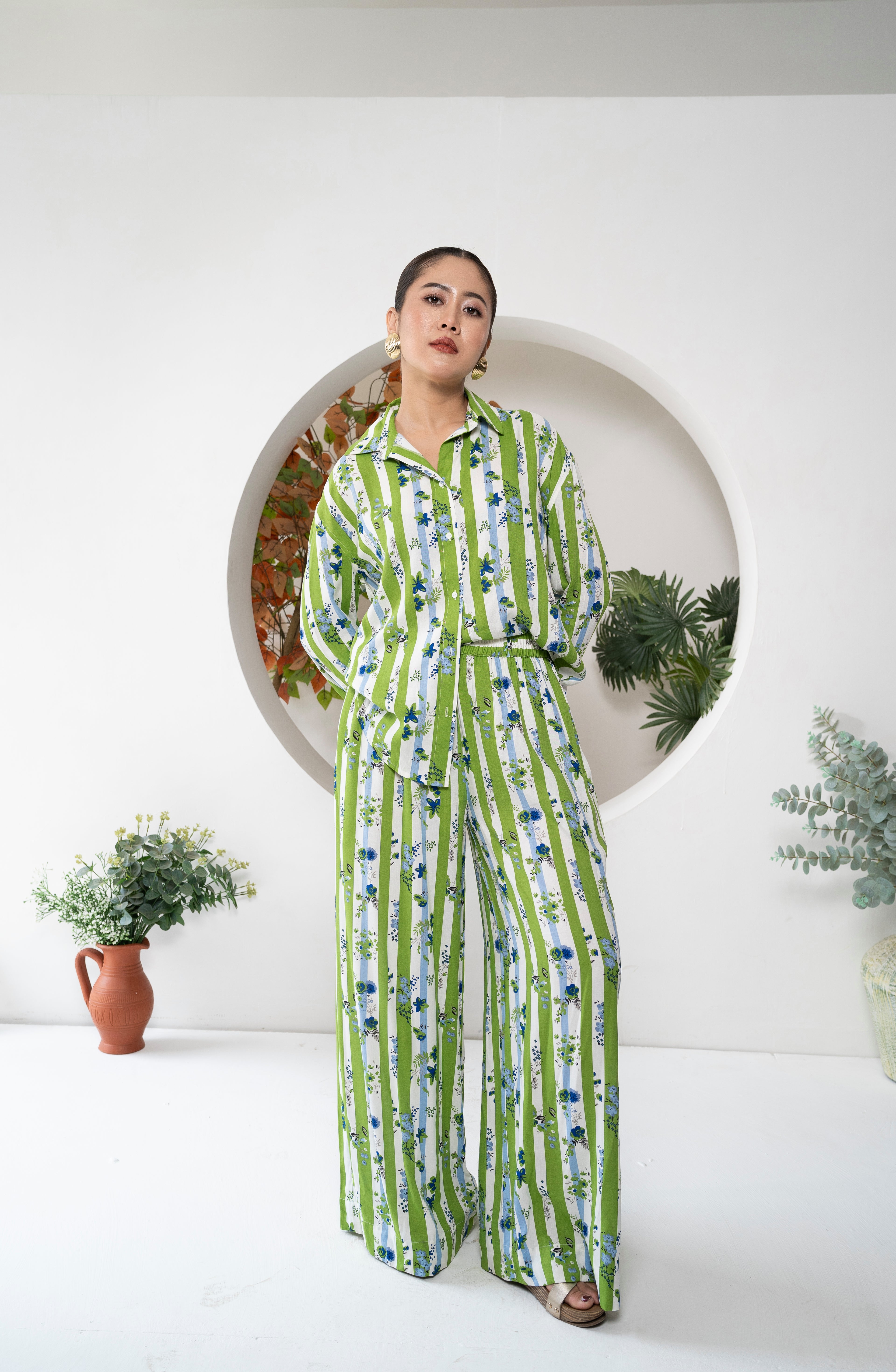 Woman wearing a green and blue striped cord set standing in front of a decorative wall with plants.