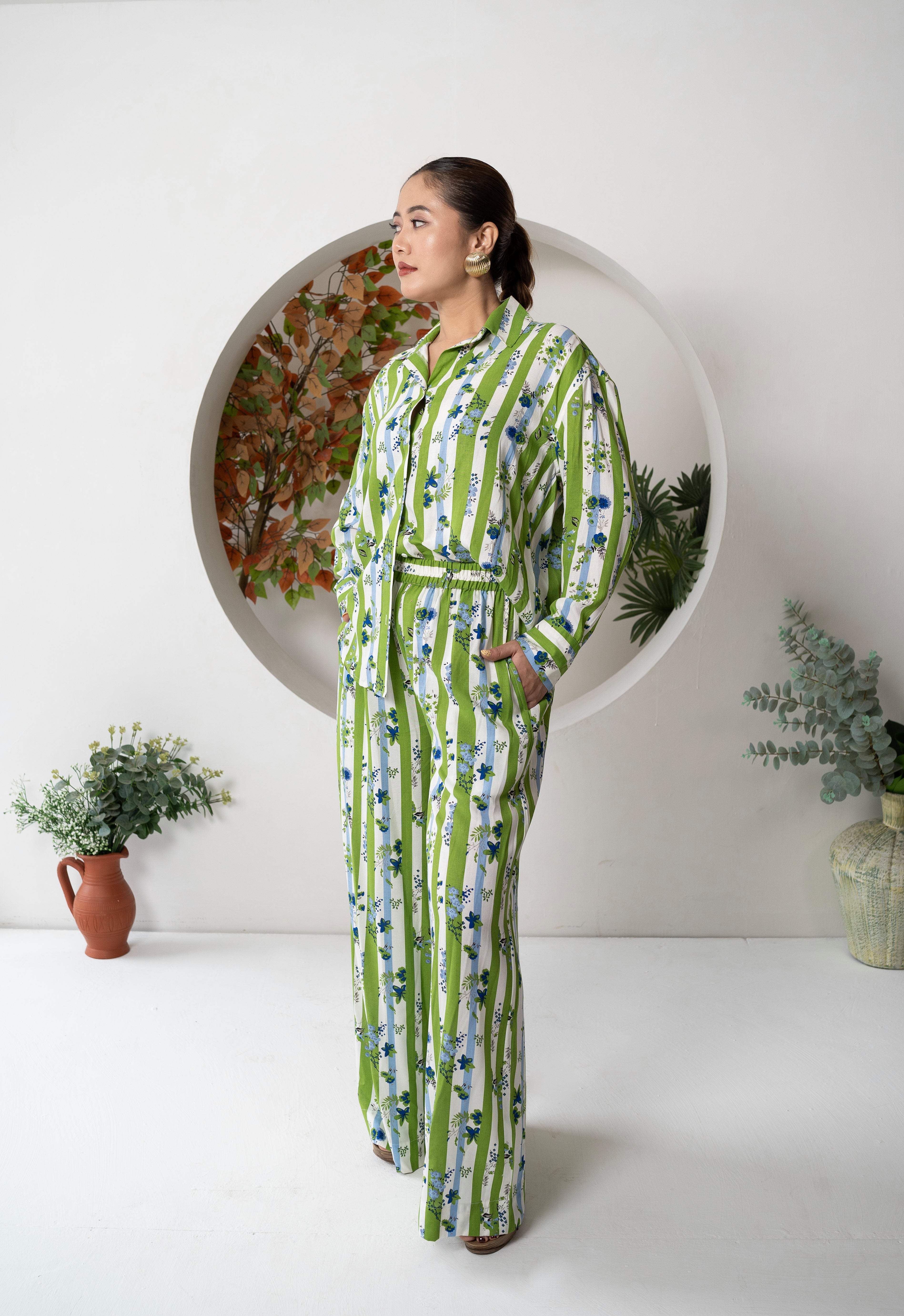 Woman wearing a green and white patterned dress standing in a minimalistic room with plants.