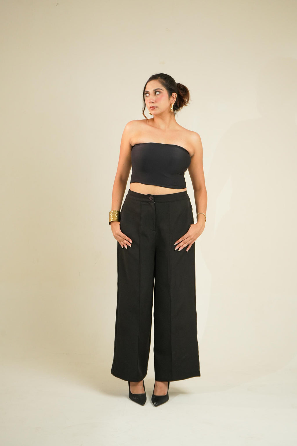 A woman modeling a vrinda black strapless tube top and matching black wide-leg pants against a plain beige studio background.