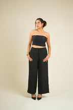 A woman modeling a vrinda black strapless tube top and matching black wide-leg pants against a plain beige studio background.