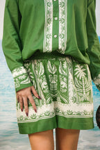 A person wearing a green and Yoshita Green Cotton Co-ord Set | Oversized Shirt & Shorts photographed against a blurred beach or water background.