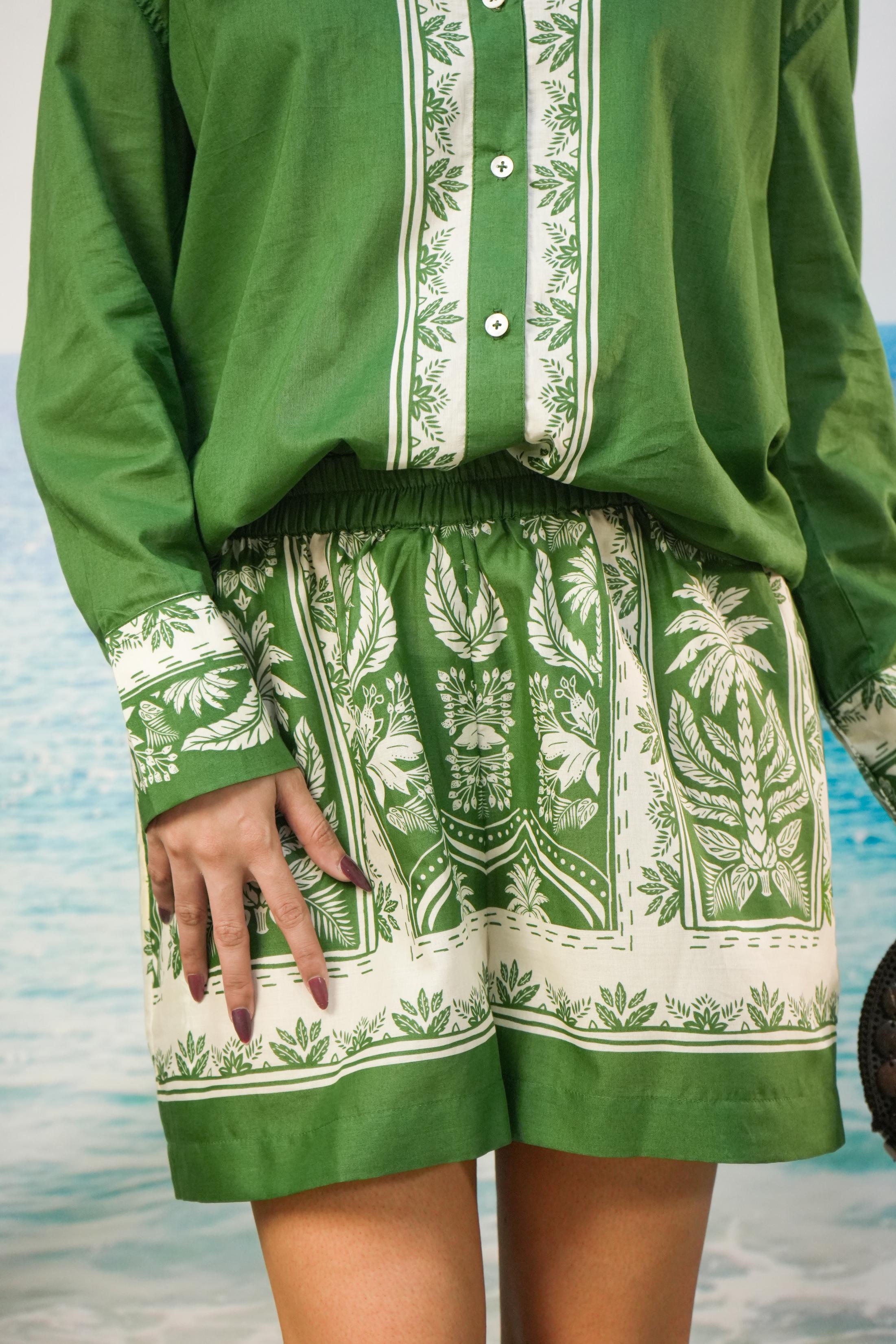 A person wearing a green and Yoshita Green Cotton Co-ord Set | Oversized Shirt & Shorts photographed against a blurred beach or water background.