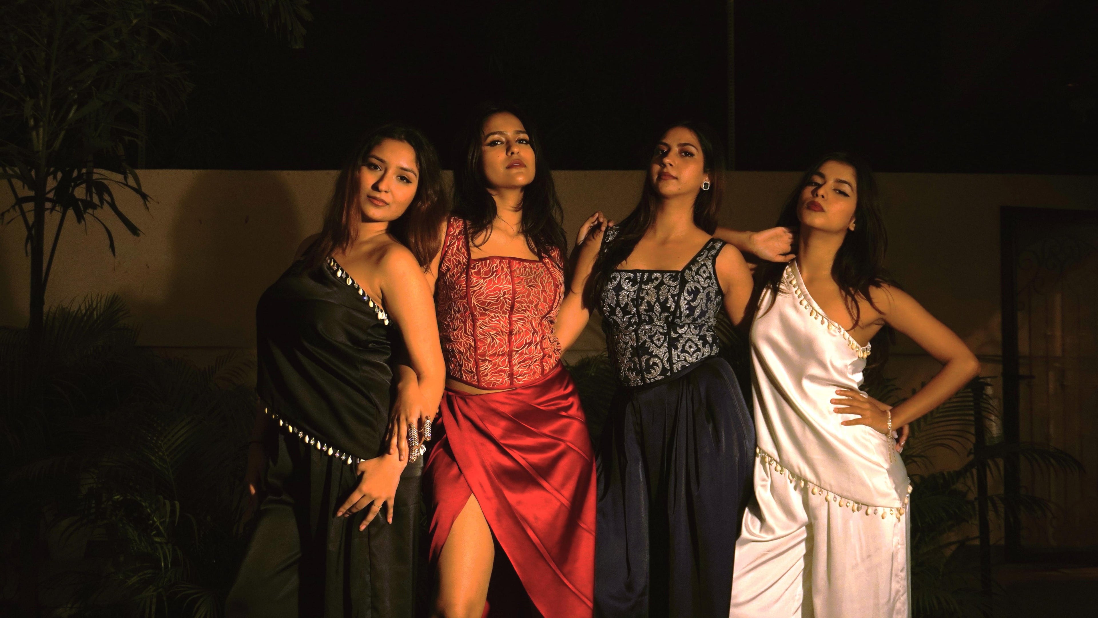 Four women in Khamna celerate edit dresses posing together against a dark background